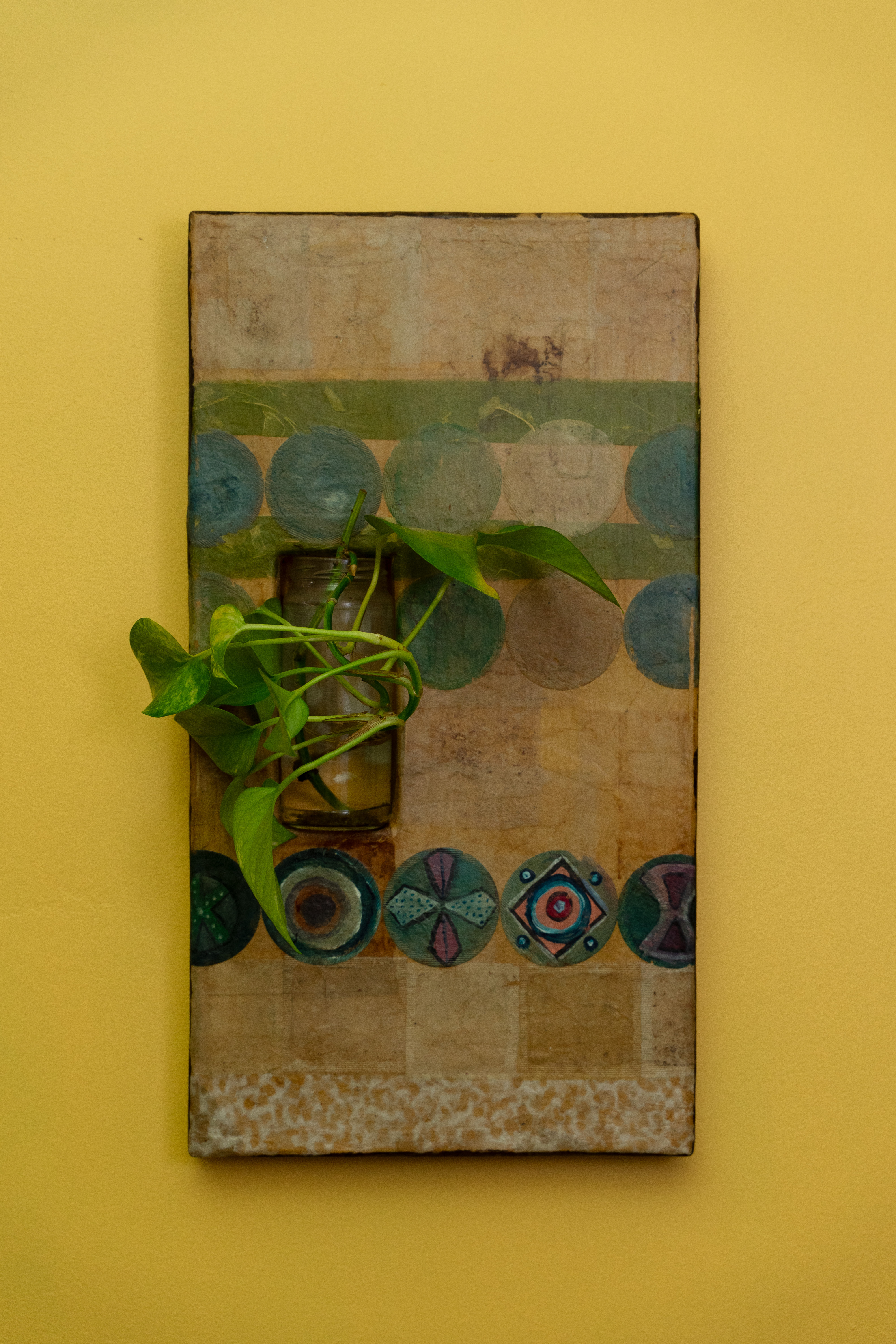 a square form with multiple designs on it, including blue circles, green lines, and decorative circles on the bottom with a jar hung on the left side holding a plant